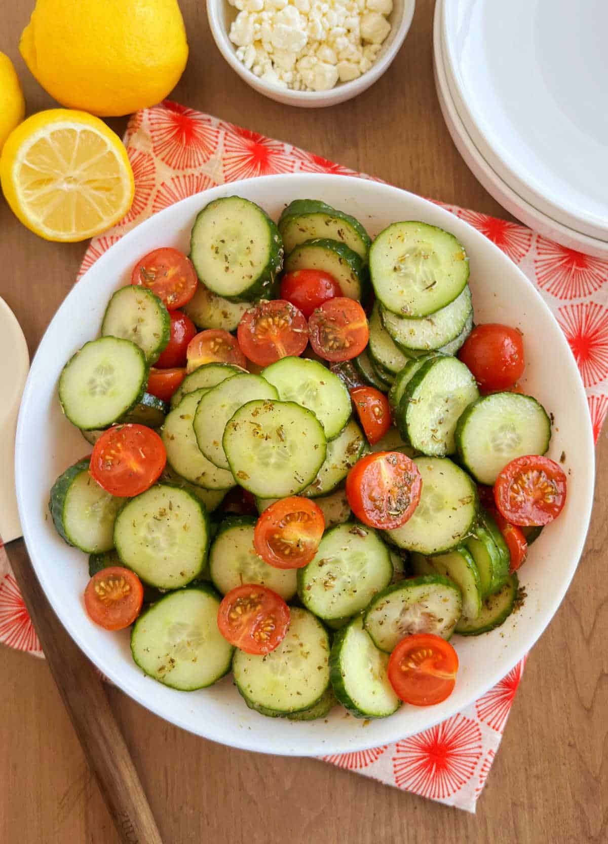 cucumber tomato salad with lemon and feta cheese in a white serving bowl.