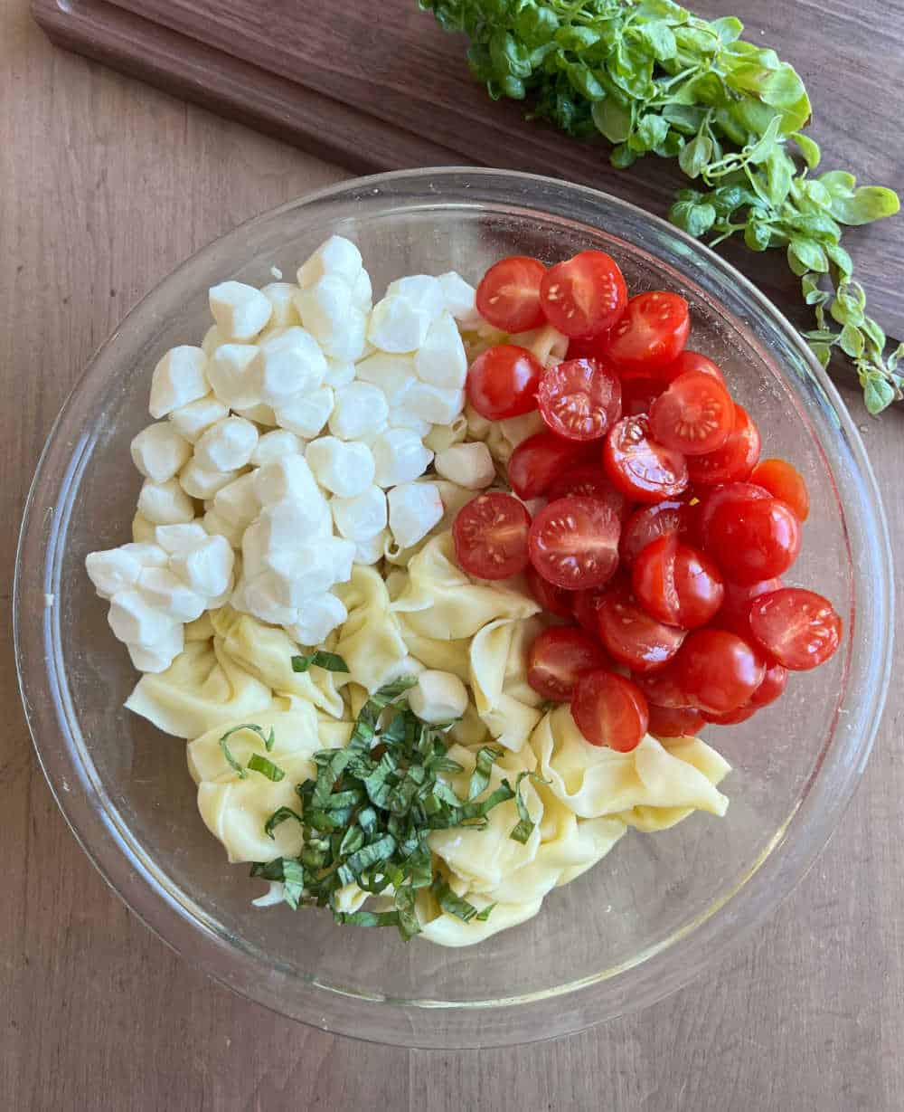 tomatoes, mozzarella, fresh basil and tortellini in mixing bowl.