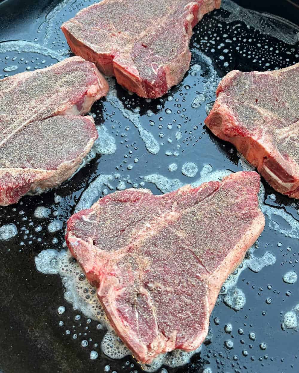 seasoned porterhouse steaks cooking on griddle.