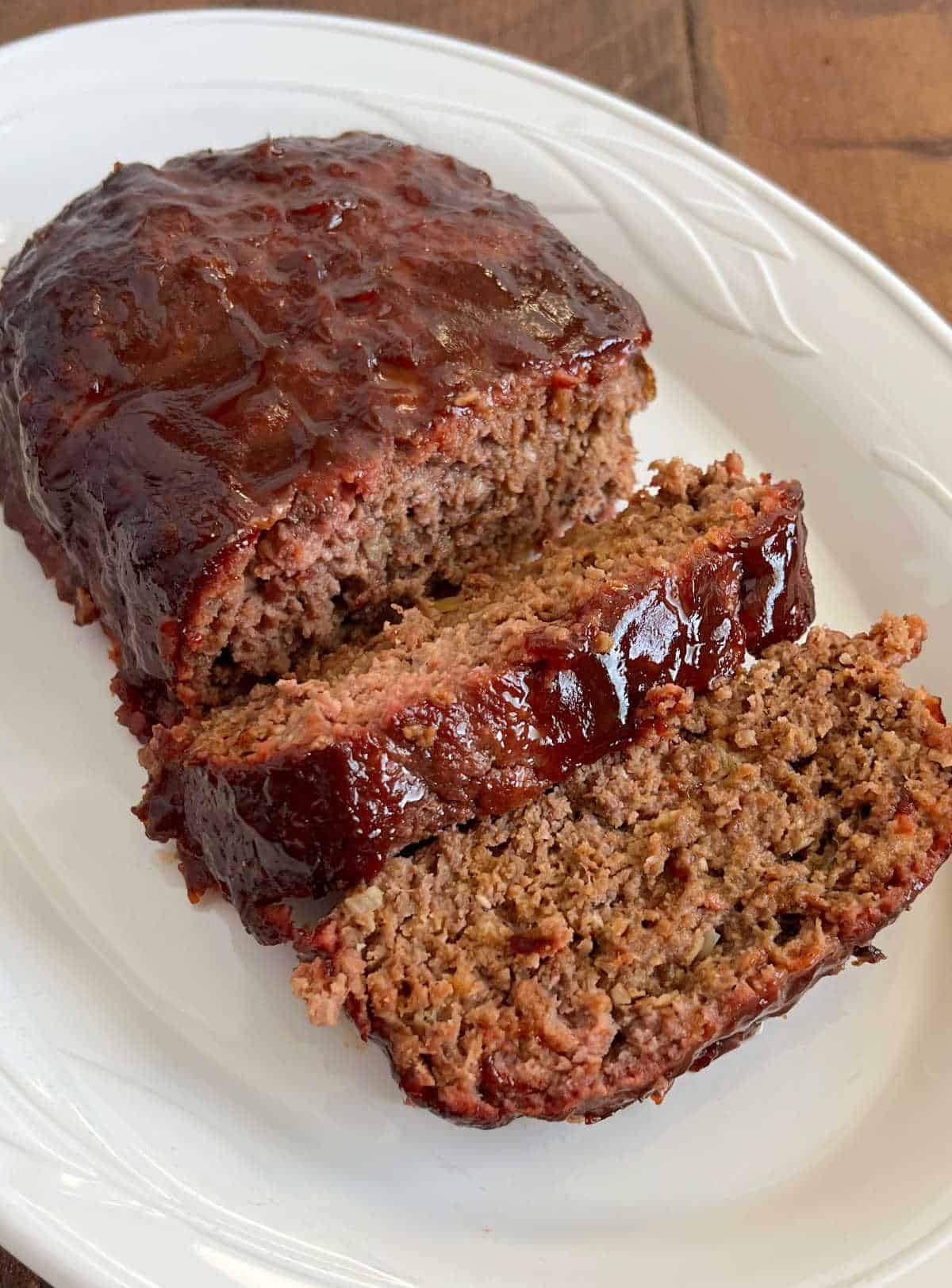 sliced smoked meatloaf with bbq glaze on white platter.