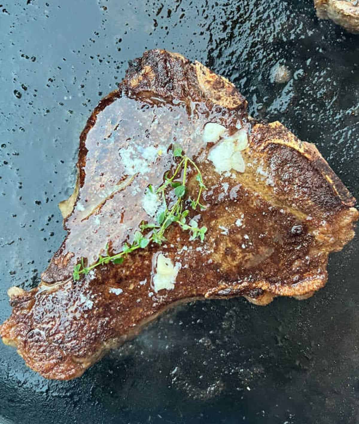 porterhouse steak with garlic butter and thyme on griddle.