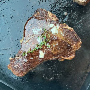 porterhouse steak on blackstone griddle with garlic butter and thyme.