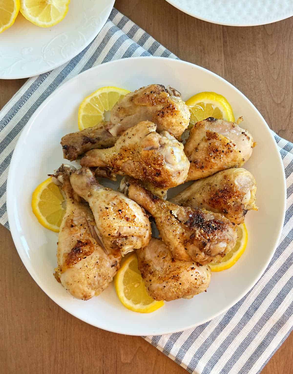 lemon pepper baked chicken legs with sliced lemons on a plate.