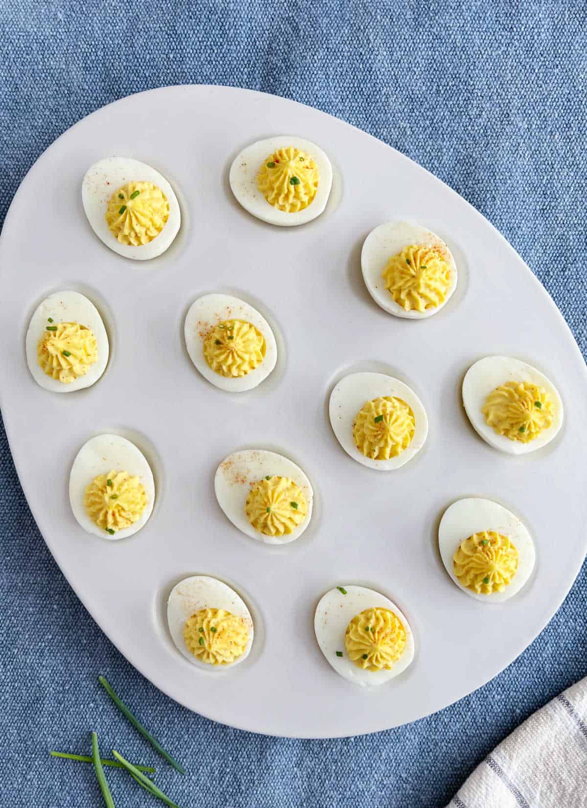 classic deviled eggs with chives and paprika in egg shaped platter.