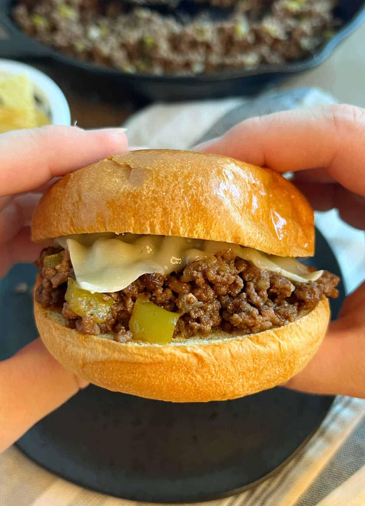 cheesesteak sloppy joe sandwich on toasted bun in hand.