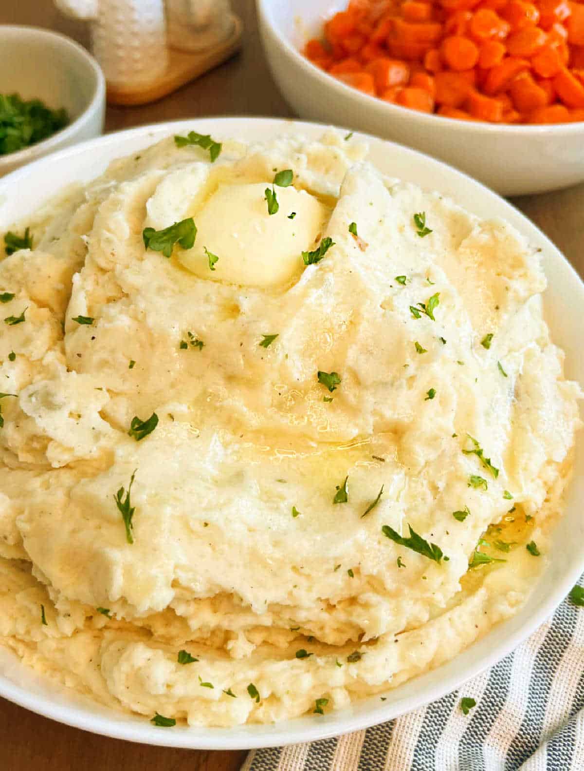 bowl of mashed potatoes with melted butter on table.