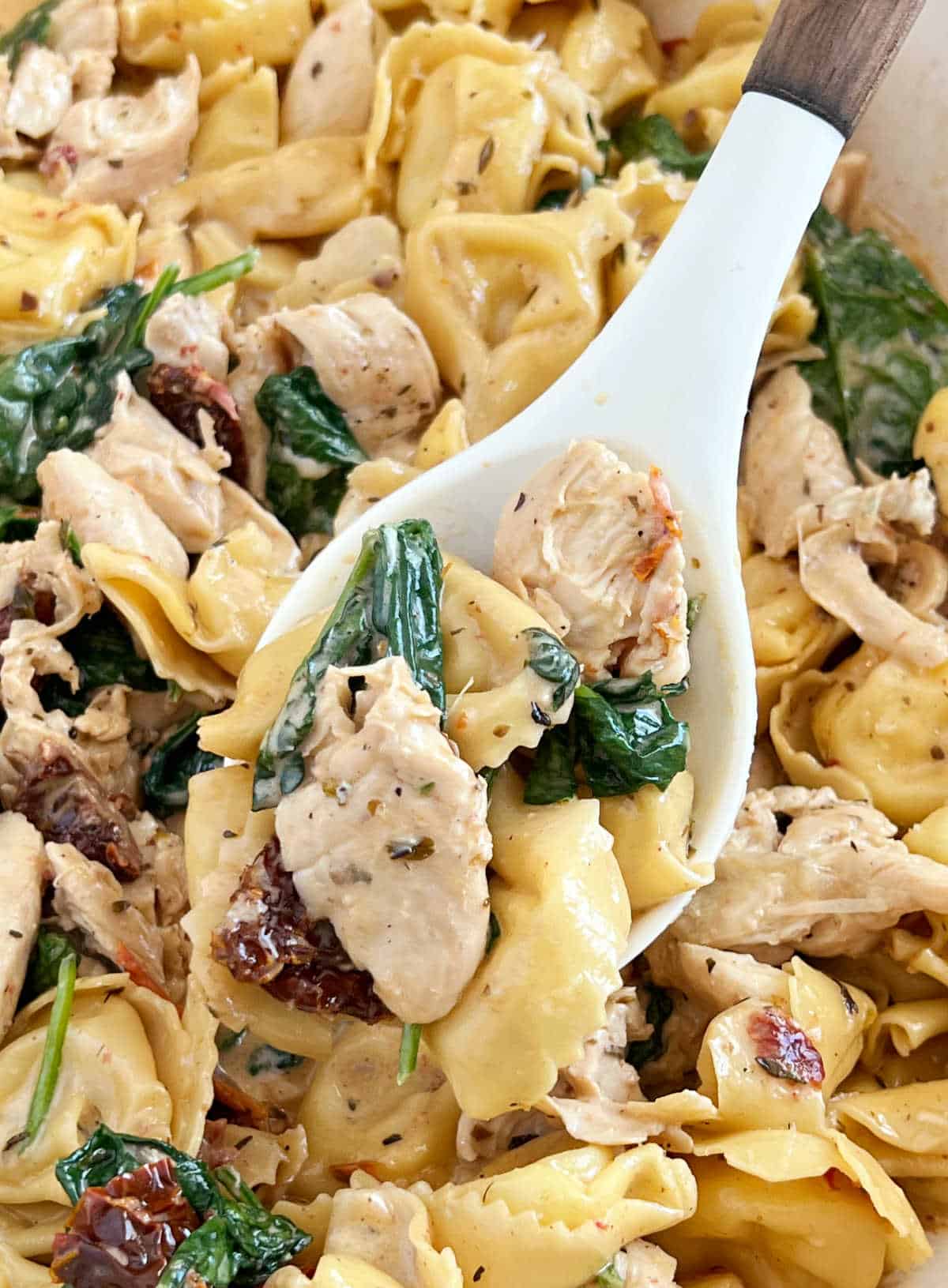 chicken and tortellini with spinach on a serving spoon.