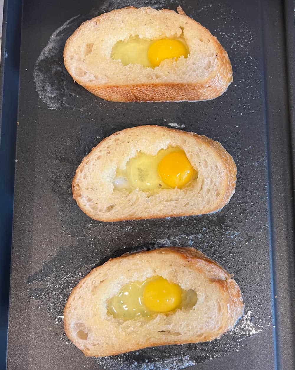 pieces of bread with egg in middle on griddle.