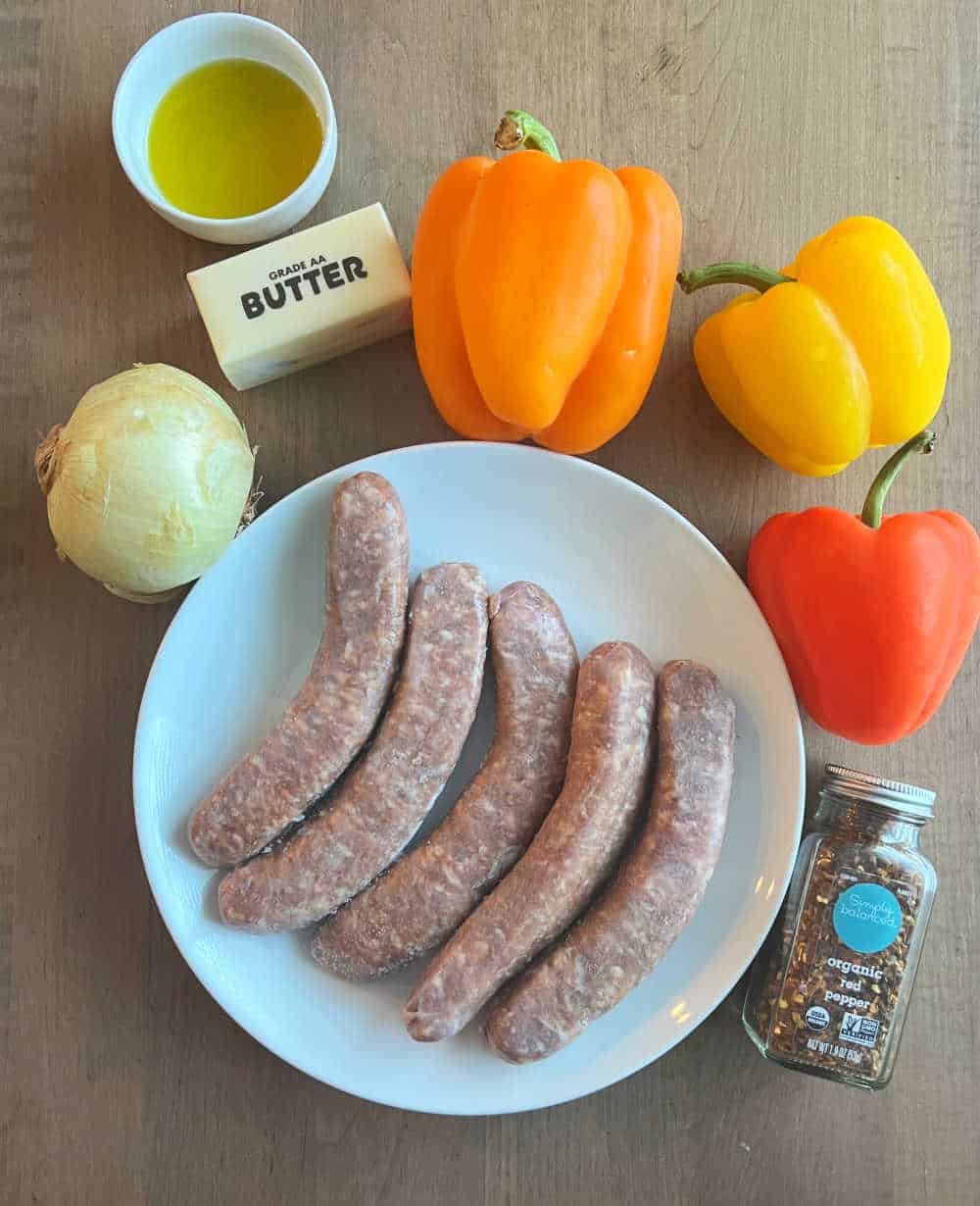 plate of sweet Italian sausages, bell peppers, yellow onion, butter, olive oil and red pepper flakes.