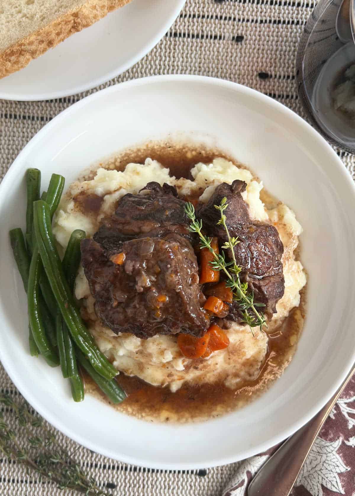 plate of braised short ribs with carrots, green beans and mashed potatoes on table.