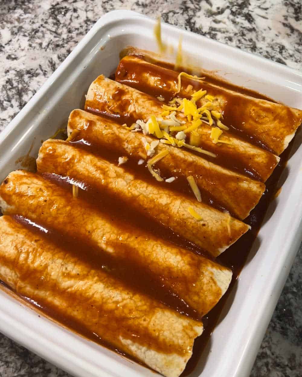 top enchiladas with sauce and cheese in baking dish.