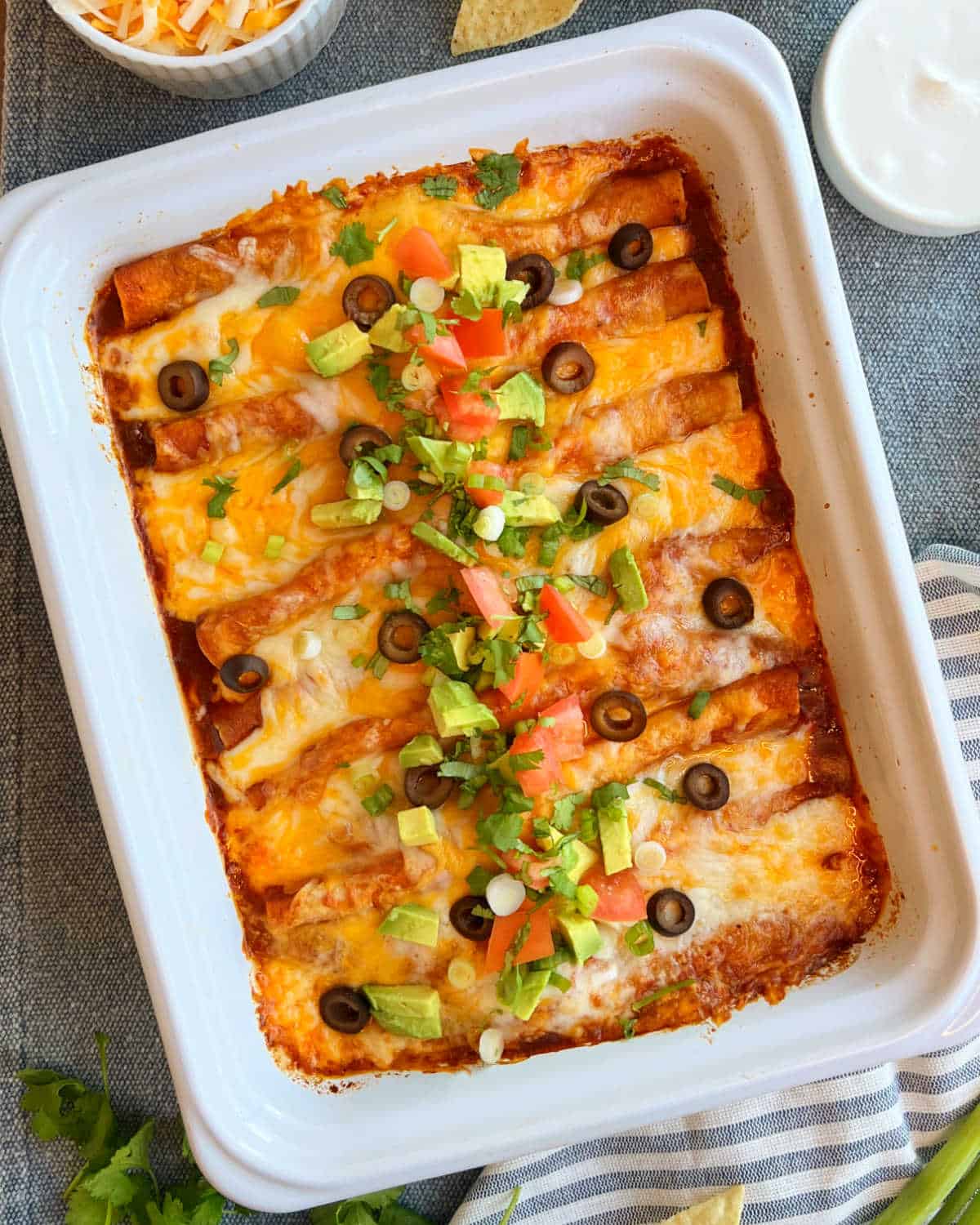 easy ground beef enchiladas with red sauce, cheese and toppings in white casserole dish.