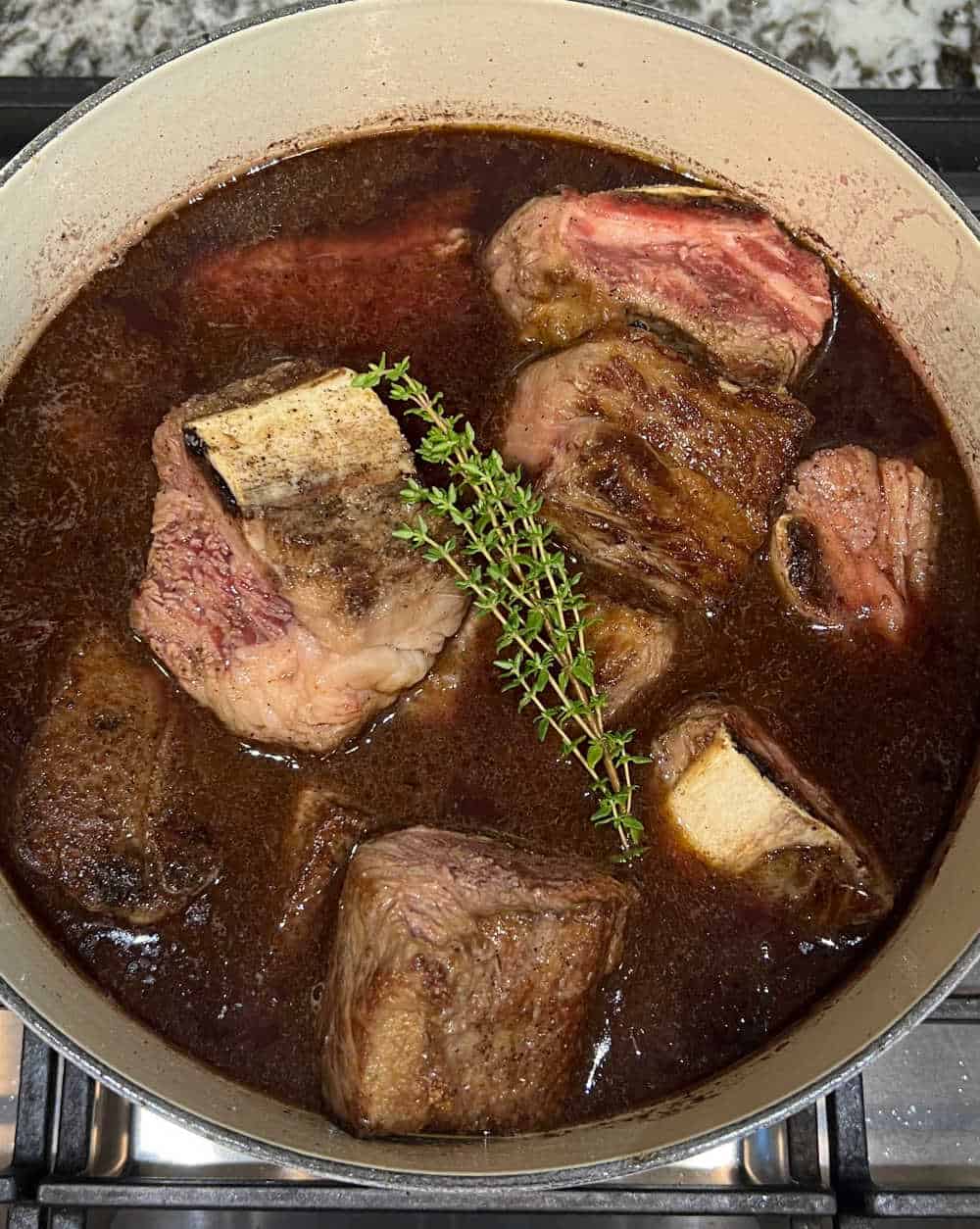 seared beef ribs in braising liquid in dutch oven.