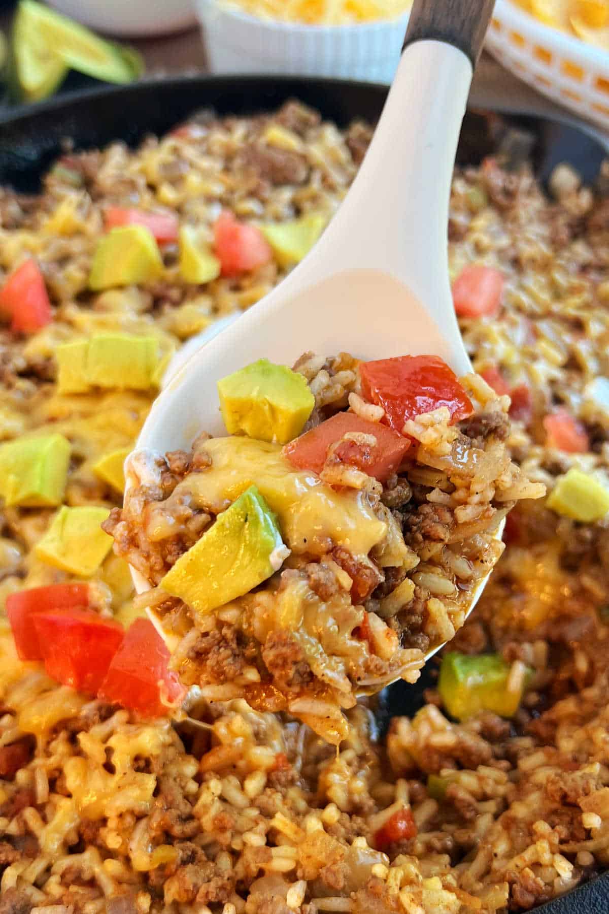 skillet taco rice with cheese, tomato and avocado in serving spoon.