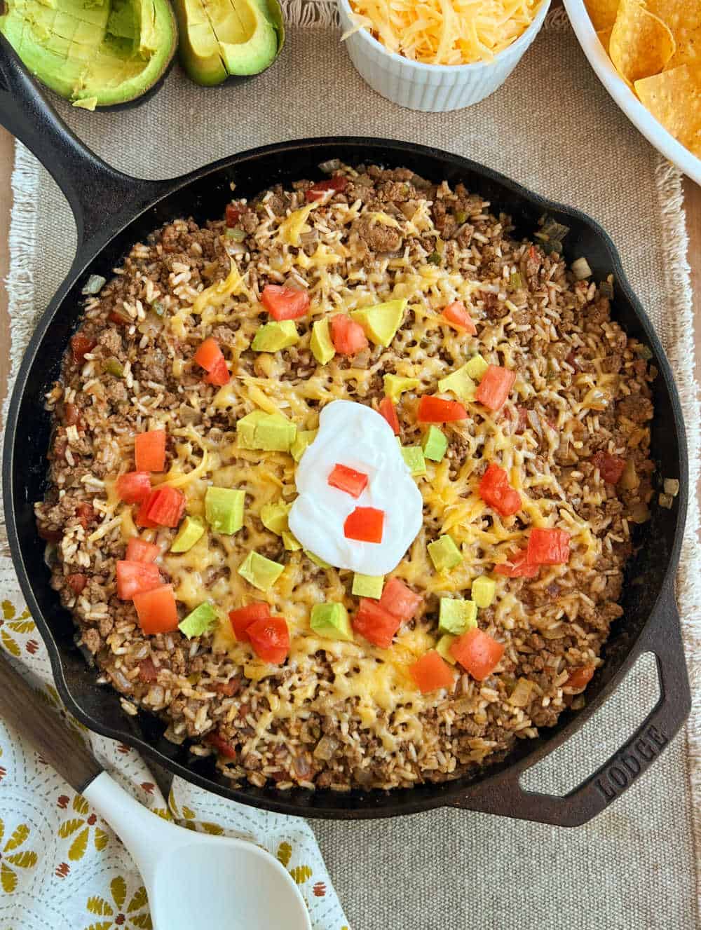 taco rice in cast iron skillet with cheese, tomatoes and avocado.