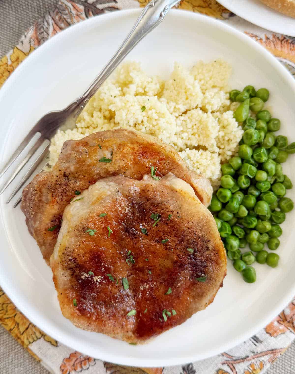 brown sugar baked pork chops with couscous and peas on a white plate.