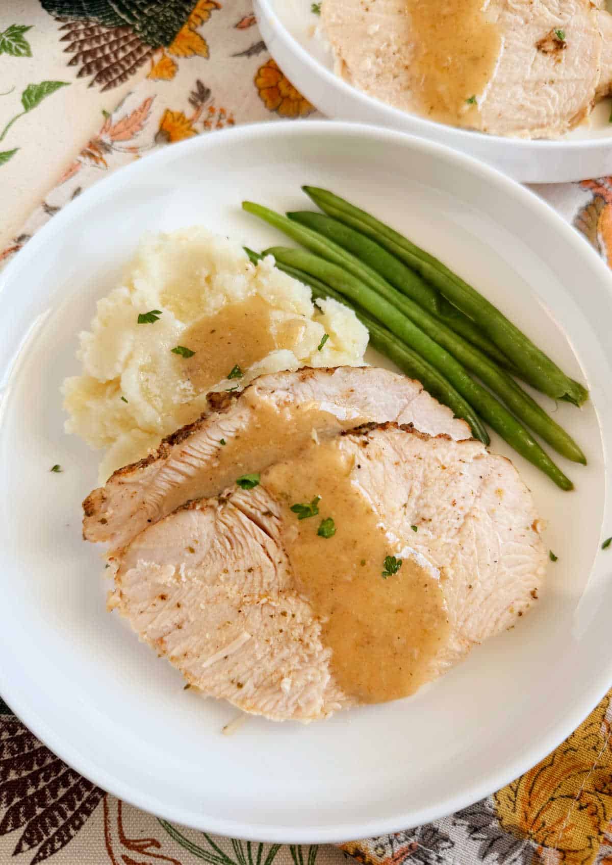 crockpot turkey breast slices on plate with mashed potatoes and green beans.