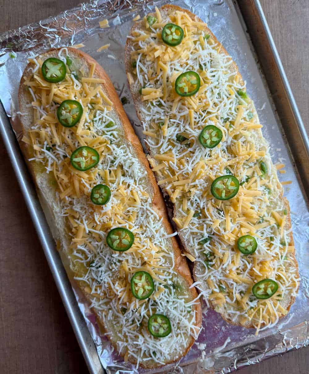 French bread halves with cheese and jalapeno peppers on baking sheet.