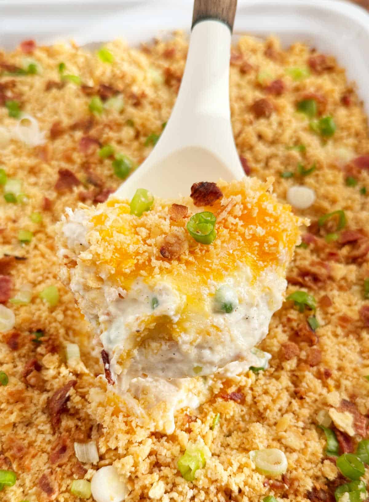 million dollar chicken casserole with green onion, bacon and peas on a serving spoon.