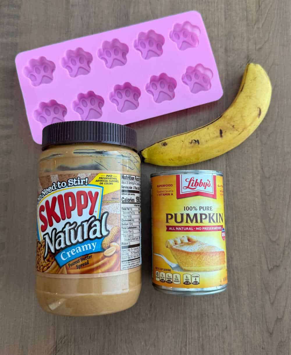 peanut butter, banana, canned pumpkin and paw print treat mold on table.