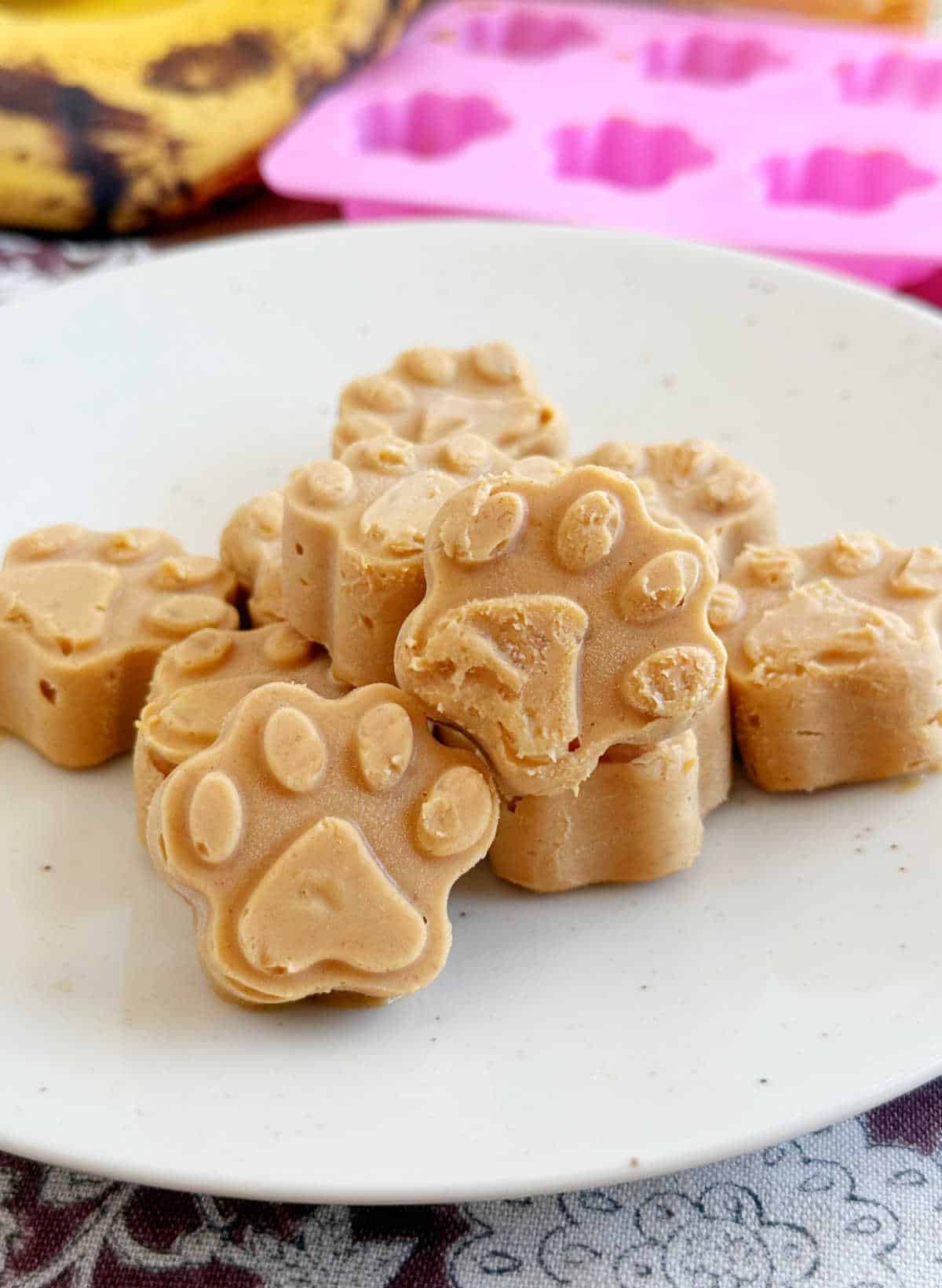 homemade peanut butter banana frozen dog treats shaped like paw print on a plate.