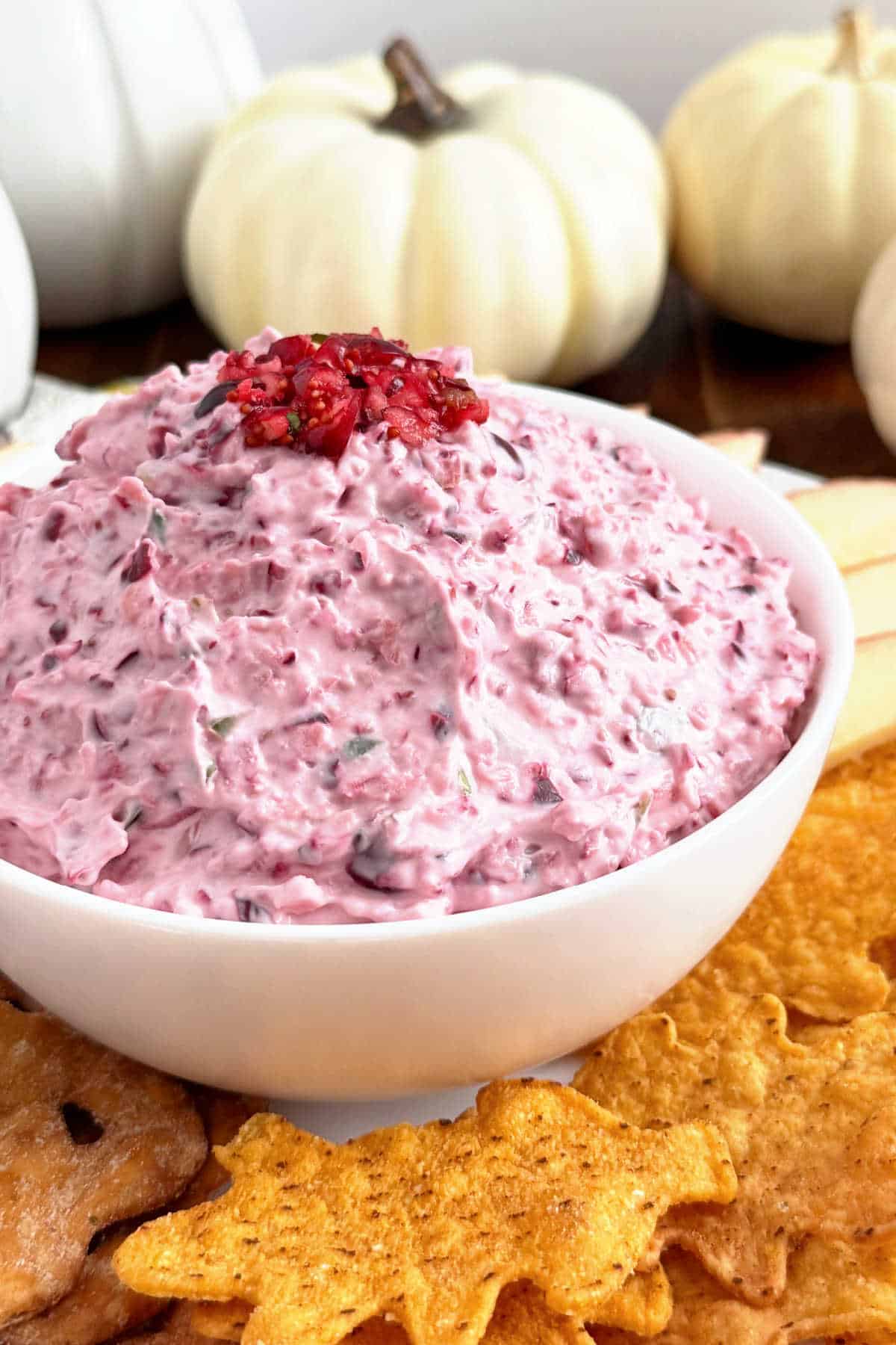 bowl of jalapeno cranberry dip with apples, tortilla chips and pretzels.