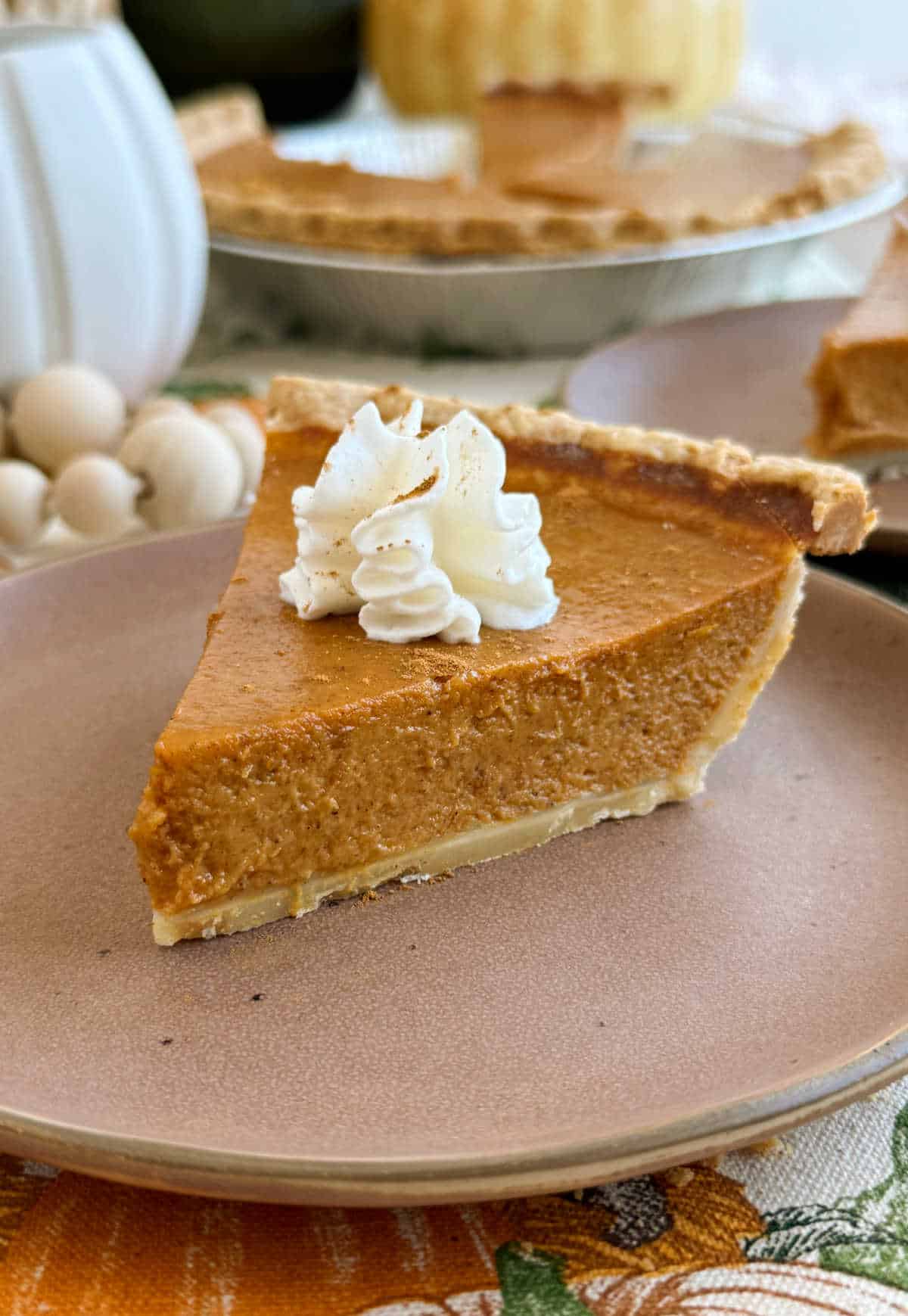 pumpkin pie slice topped with whipped cream on plate.