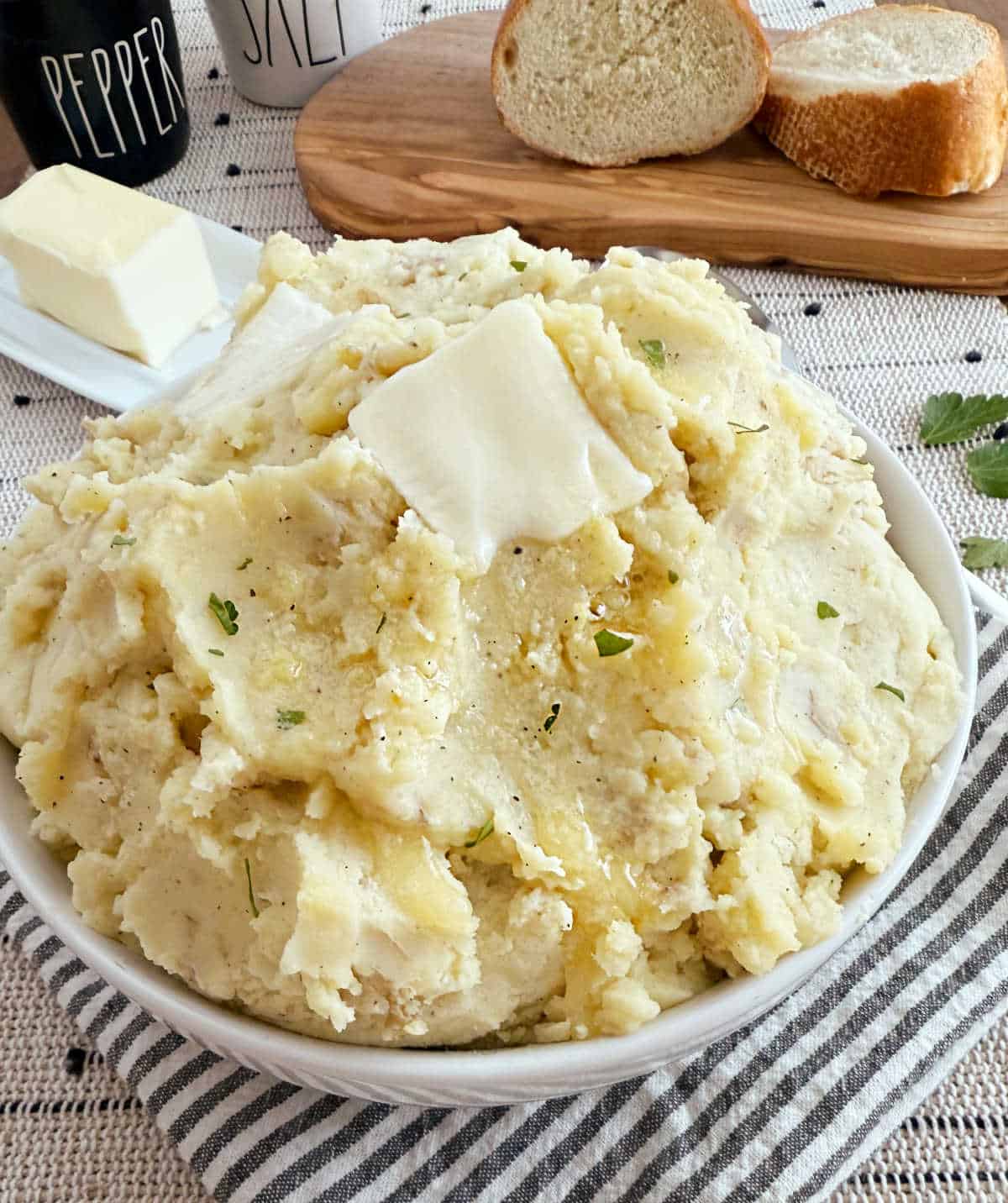 bowl of rustic mashed potatoes with skin on and pat of butte on top.