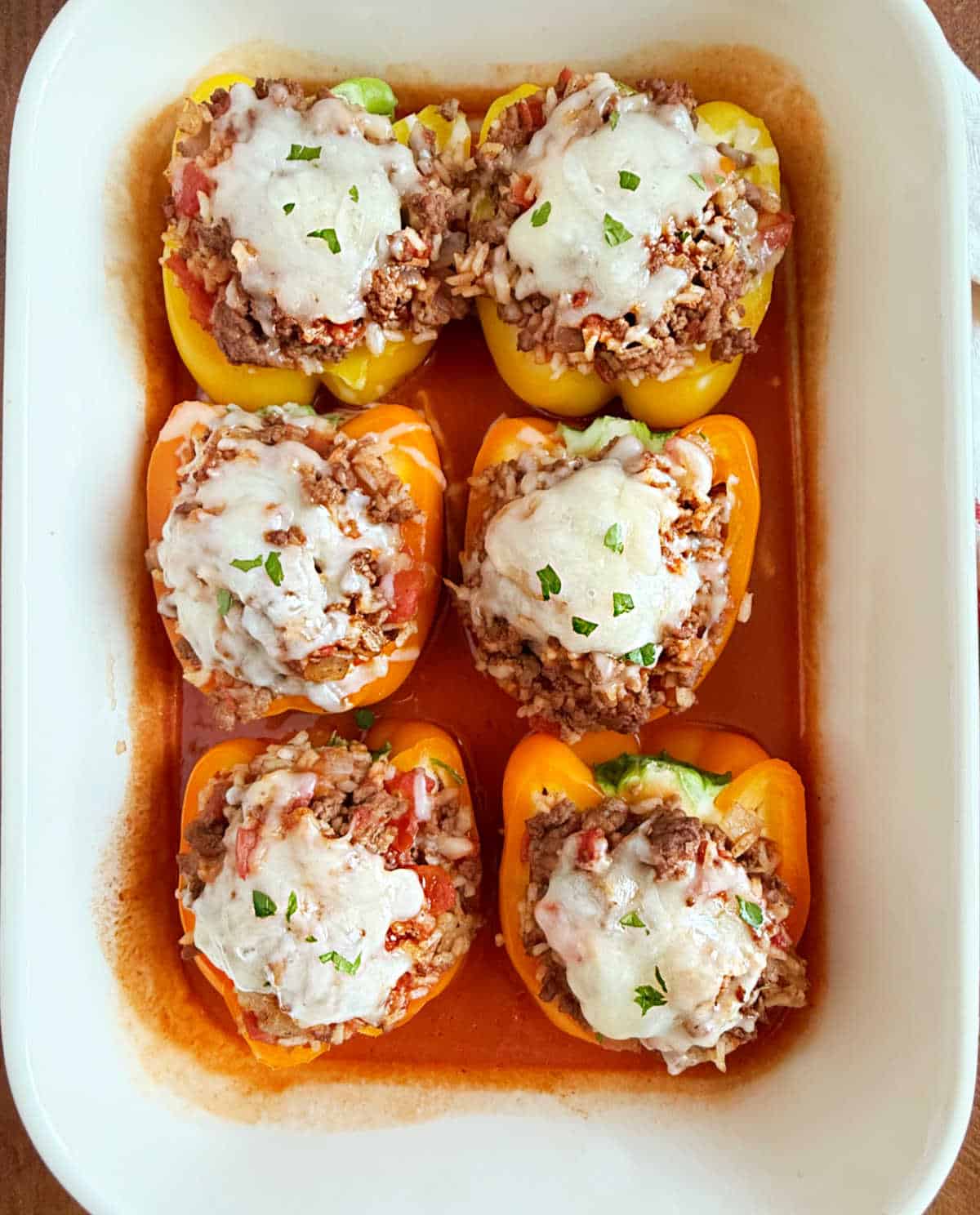 bell peppers stuffed with beef and rice with tomato sauce in baking dish.