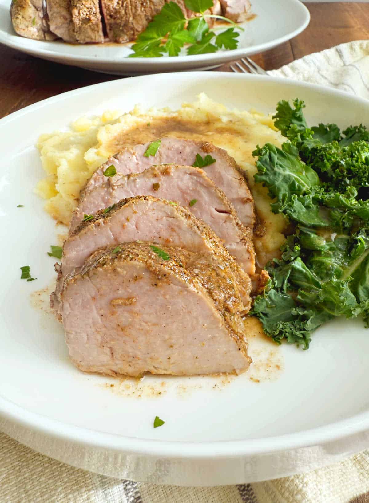 sliced baked pork tenderloin with mashed potatoes on a white plate.