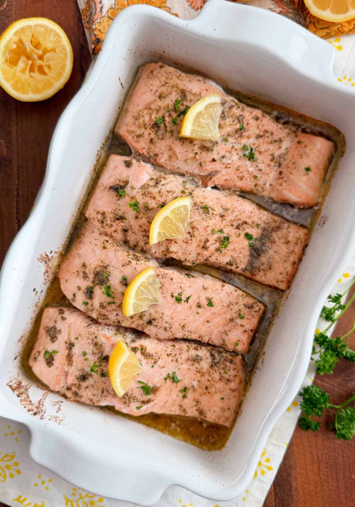 baked salmon with lemon slices in garlic butter in baking dish.