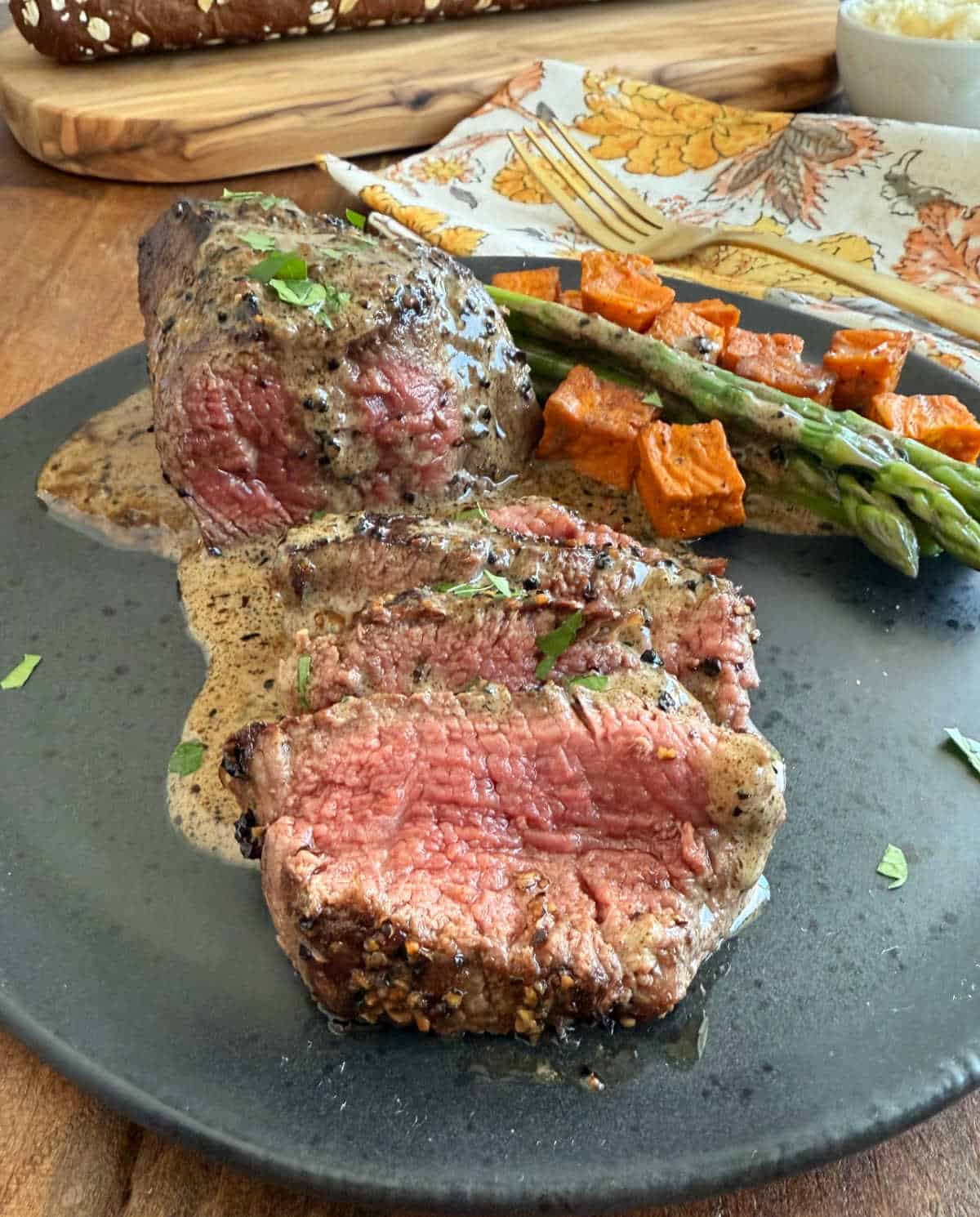 sliced steak au poivre in bourbon cream sauce on plate with vegetables.