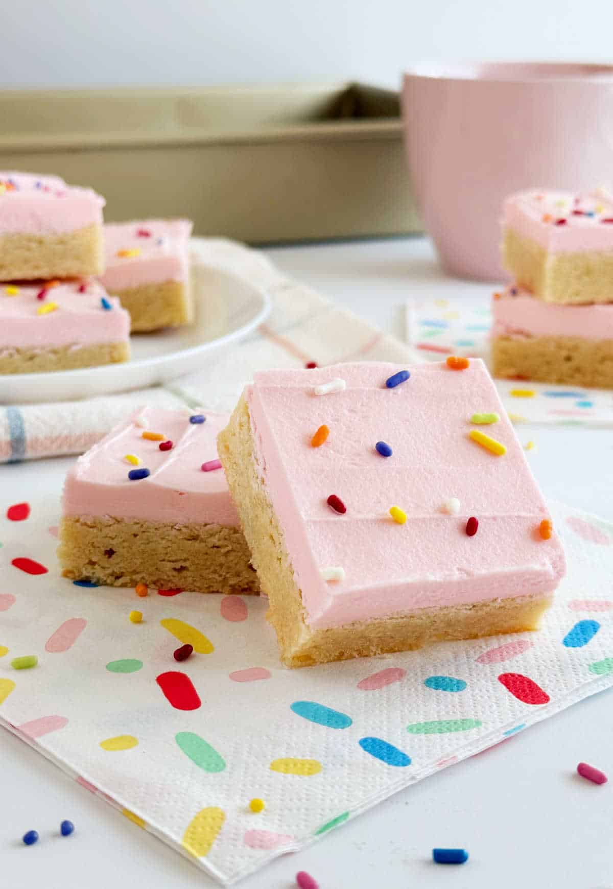 sliced sugar cookie bars with pink frosting and sprinkles on the table.